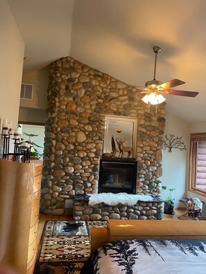A stone fireplace with a mirror above it, a ceiling fan, and a patterned rug on the floor. - Barrel sauna, two plug-play hot tubs ,pool table Mt View private trail to river  (Arlington)
