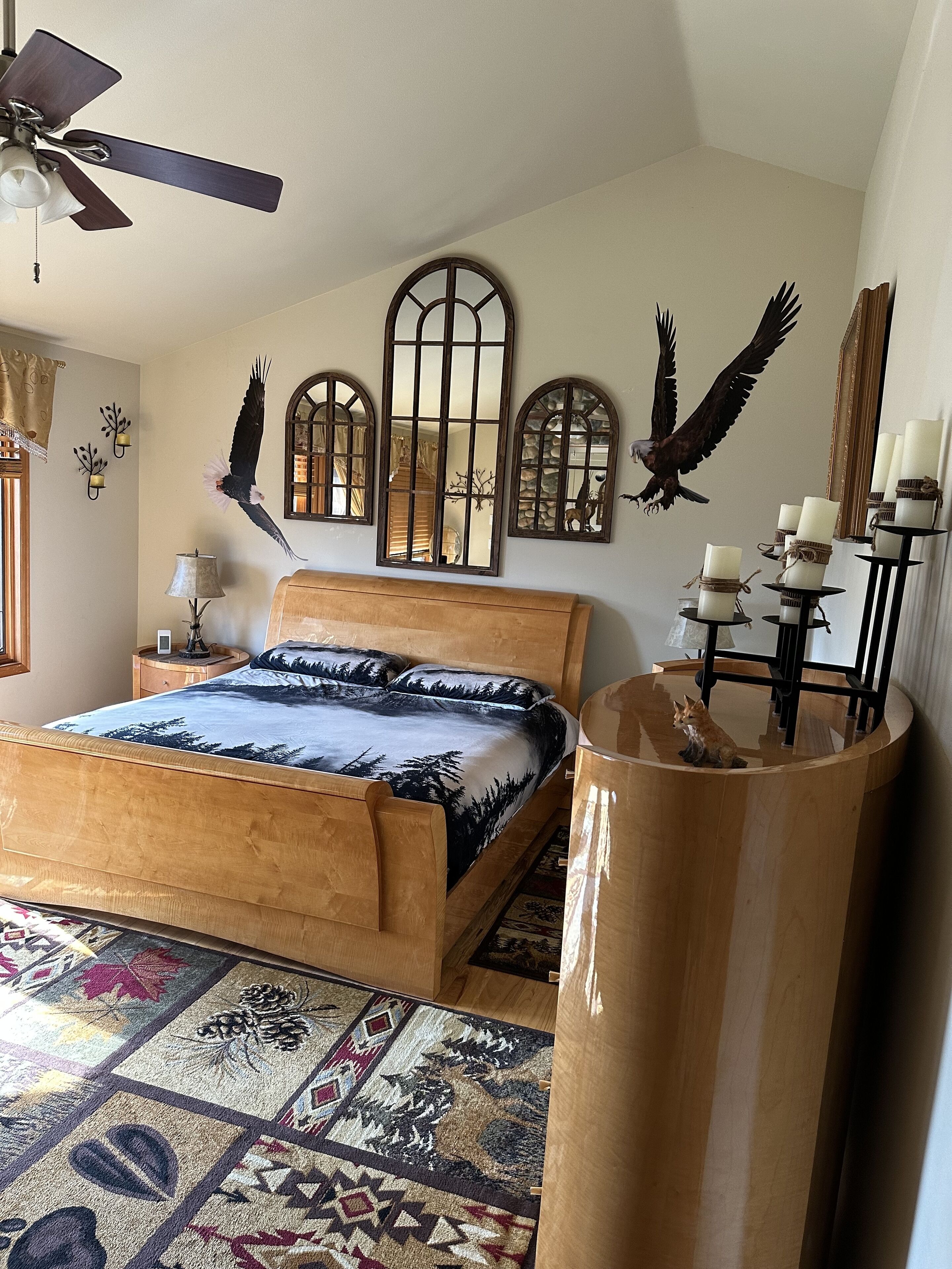 A bedroom with a wooden bed, a ceiling fan, wall-mounted mirrors, and a decorative fox statue.