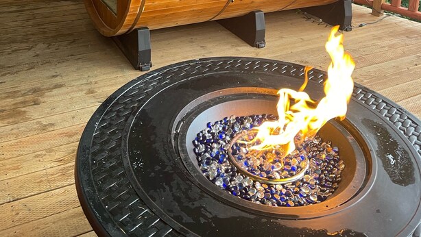 A wooden cabin with a sloped roof and a fire pit with blue and clear glass pebbles.