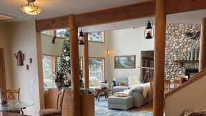 A spacious living area with a wooden dining table, a sofa, and a fireplace. There is a Christmas tree and a stone wall in the background.