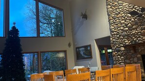 A spacious dining area with a stone fireplace, large windows, and a Christmas tree.