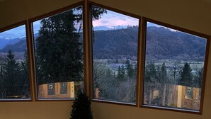 A room with a large window overlooking a mountainous landscape, a ceiling fan, and a Christmas tree.
