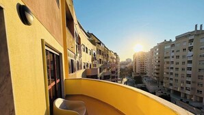 Un balcon avec un mur jaune incurvé, une fenêtre et une chaise.