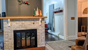 A living room with a fireplace, a ceiling fan, and a wooden shelf with decorative items. - Family Friendly FULL HOUSE (Warren)
