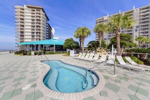 A swimming pool with a tiled deck, lounge chairs, palm trees, and high-rise buildings in the background.