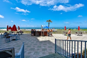 A beachside patio with outdoor seating, a bar, and a view of the ocean.