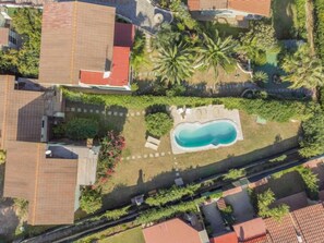 An aerial view of a residential area with a swimming pool surrounded by greenery and a few houses.