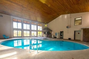 An indoor swimming pool with a wooden ceiling, large windows, and a lifeguard chair. - Cole's Condo: Comfort, Cozy, Convenient (Pigeon Forge)