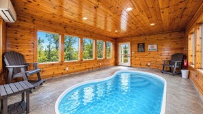 Een binnenzwembad met houten wanden en ramen, twee Adirondack-stoelen, en een bord waarop staat dat rijden niet is toegestaan tijdens verblijf in de chalet.