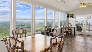 Ein Essbereich mit großem Tisch und Stühlen, großen Fenstern mit Blick auf die Landschaft und einem Deckenventilator.