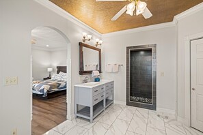 Een moderne badkamer met een witte wastafel, een grote spiegel en een douchecabine betegeld met zwart.