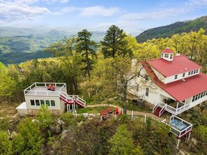 Een chalet met een rood dak en witte muren, omgeven door bomen en een bergachtig landschap.