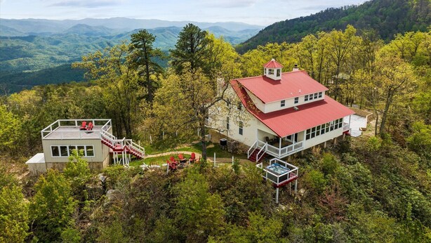 Eine zweistöckige Holzhütte mit rotem Dach, umgeben von dichtem Wald und Bergen im Hintergrund.