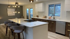 A modern kitchen with a central island, bar stools, pendant lighting, and a view of the outdoors.