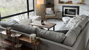 A modern living room with a large window, a fireplace, and a flat-screen TV mounted on the wall.
