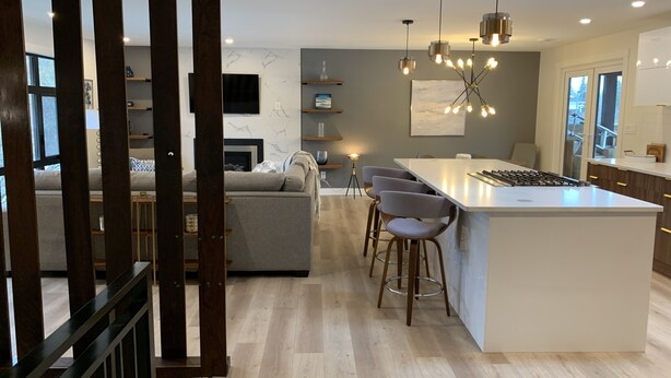 A modern kitchen with a central island, bar stools, pendant lighting, and a view to the living area.