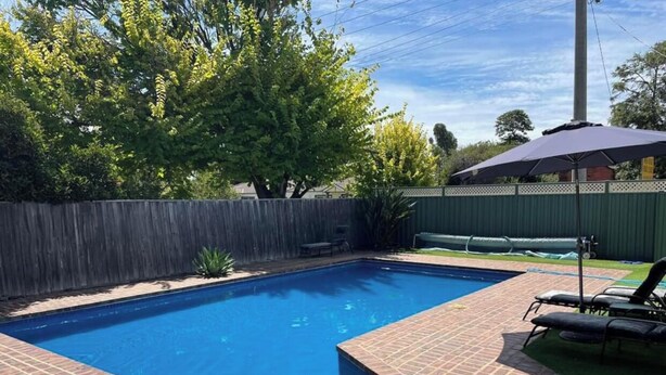 A rectangular swimming pool with a brick border, surrounded by a wooden fence and green grass. - Hidden Oasis on Piper.  Park your car and walk to everything (Yarrawonga)