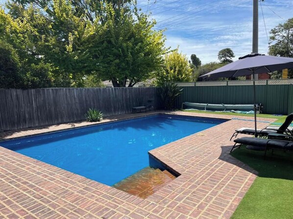 Relax by the pool surrounded by lush greenery and a brick border.