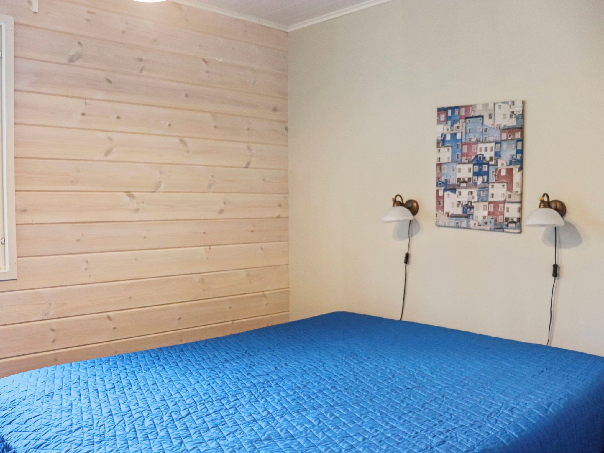 A room with a blue quilted bedspread, wooden panel walls, and two wall-mounted lamps.