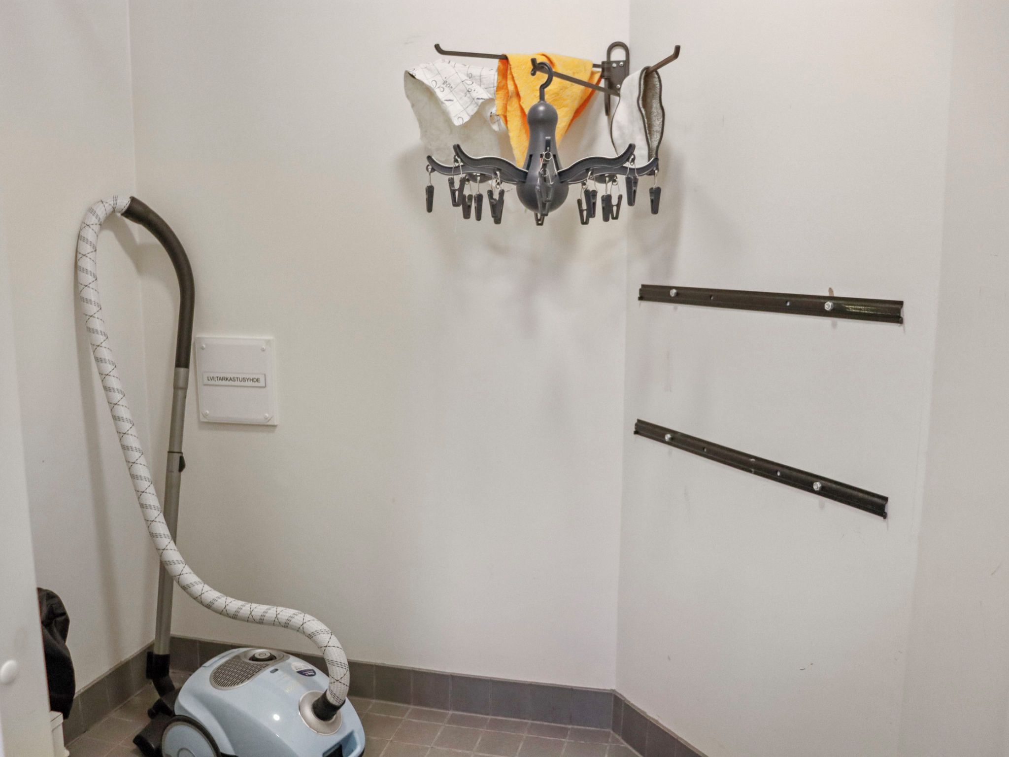 A bathroom with a vacuum cleaner, a towel rack with towels, and a sign on the wall.