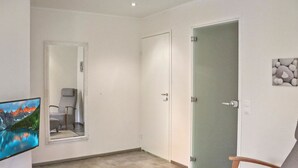 Una habitació amb televisió que mostra un paisatge de muntanya, una cadira, una porta i un objecte decoratiu petit a la paret.