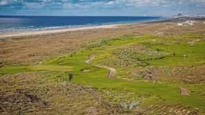 A golf course with a coastal view, a sandy beach, and a distant building. - Luxury townhome with games, high-speed WiFi, pool access, AC & beach service (Port Aransas)
