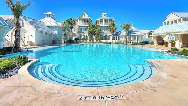 A swimming pool with a 2 ft 6 in no diving sign, surrounded by buildings with a light blue roof and white walls. - Luxury townhome with games, high-speed WiFi, pool access, AC & beach service (Port Aransas)