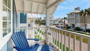 A covered balcony with a blue chair, white railings, and a view of a residential area with houses and palm trees. - Luxury townhome with games, high-speed WiFi, pool access, AC & beach service (Port Aransas)