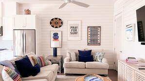 A modern kitchen with white cabinetry, a stainless steel refrigerator, and a dining area with a wicker table and a blue and white patterned bowl. - Townhouse + loft with private balcony, heated pool, gym, beach access & W/D (Port Aransas)