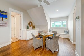 A dining area with a wooden table and wicker chairs, a ceiling fan, and a window with a view of buildings. - Townhouse + loft with private balcony, heated pool, gym, beach access & W/D (Port Aransas)