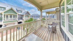 A covered porch with a table and chairs, overlooking a row of houses with green roofs and white railings. - Townhouse + loft with private balcony, heated pool, gym, beach access & W/D (Port Aransas)