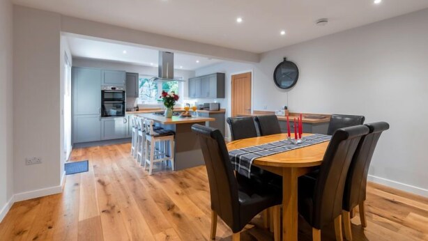 Une cuisine moderne avec des meubles gris, un îlot central et un coin repas comprenant une table en bois et des chaises noires.