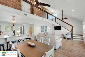 A spacious living area with a dining table, white furniture, and a staircase leading to an upper level.