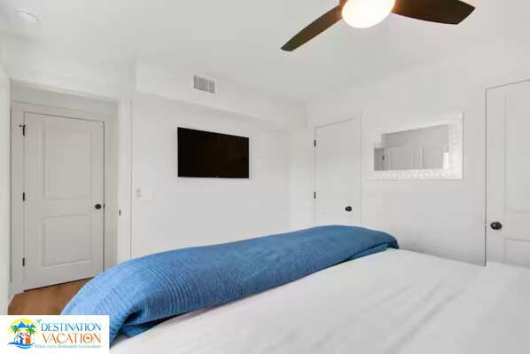 A hotel room with a bed, a ceiling fan, a television, and a mirror.