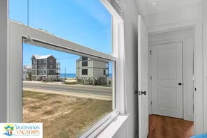 A room with a large window offering a view of a beach and buildings.