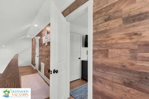 A hallway with wooden flooring, white walls, and a door leading to a room with a television. - Beachfront Bliss 3BR Home | Walk to Sand | Sleeps 10 (Port Saint Joe)