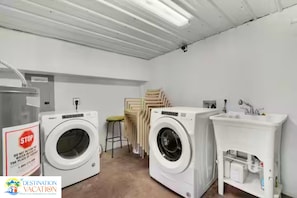 A laundry room with two washing machines, a sink, and stacked chairs.
