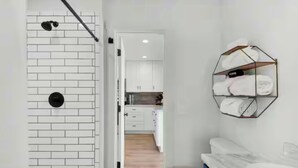 A hallway leading to a bathroom with a white brick wall, a towel rack, and a door to a kitchen area. - Steps to the Beach 3BR Coastal Home Sleeps 10 (Port Saint Joe)
