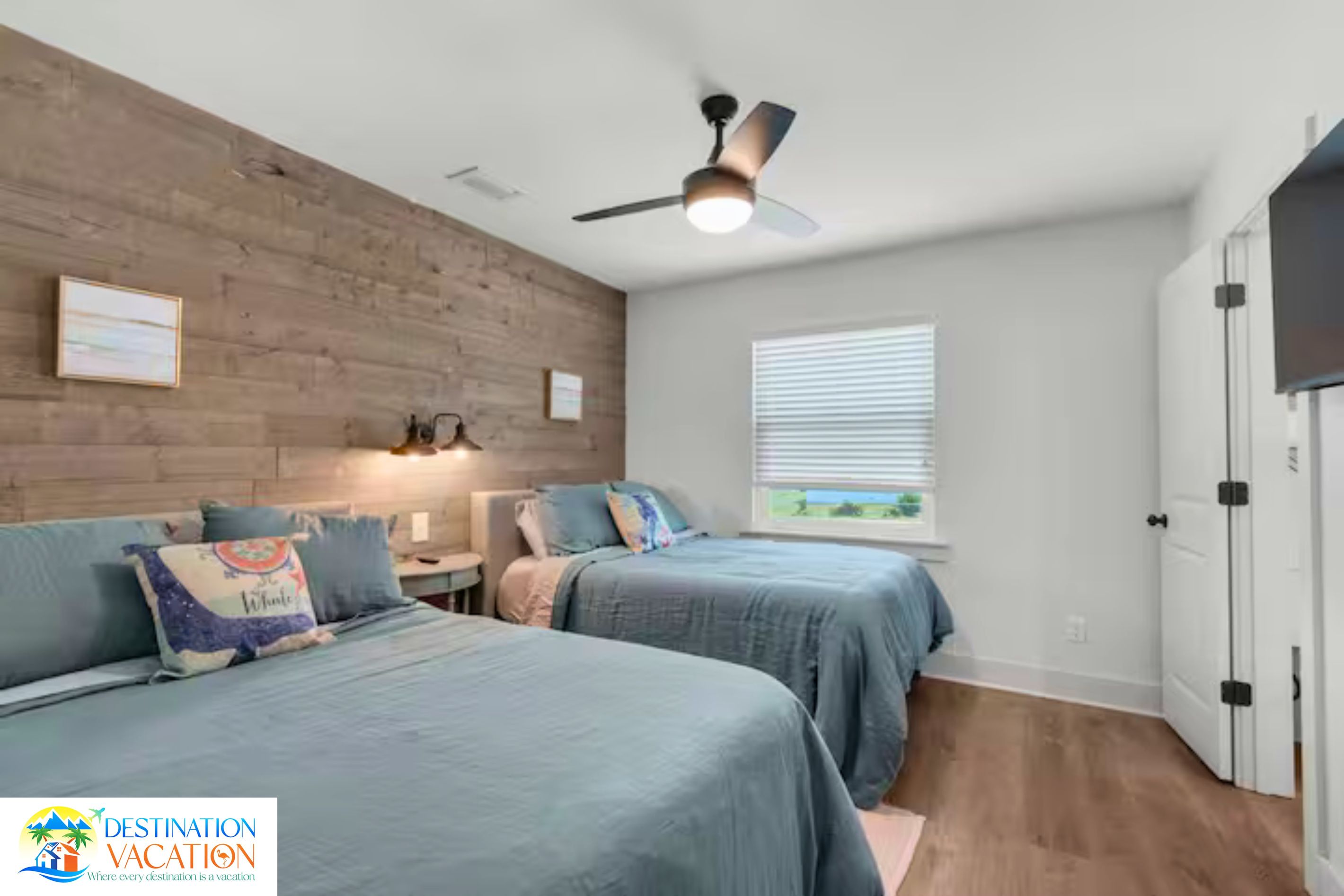 A bedroom with two beds, a ceiling fan, a window with blinds, and a door.