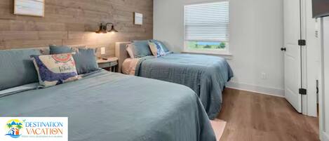 A bedroom with two beds, a ceiling fan, a window with blinds, and a door.