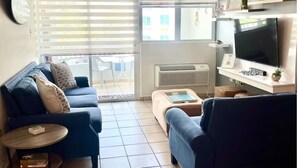 A living room with a blue sofa, a small round table, and a TV on a stand. - Gated condo, pool, high speed Wi-fi, washer & dryer. Walk to beach, near town  (Rincon)