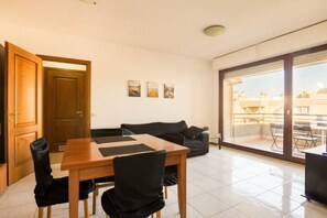 Un salon moderne avec une table à manger en bois, des chaises noires, un canapé noir et une grande porte-fenêtre coulissante donnant sur un balcon extérieur.
