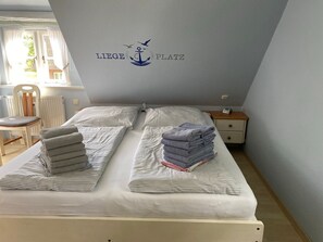 Una habitación con dos camas, una silla, una mesita de noche y una pared con un logo.
