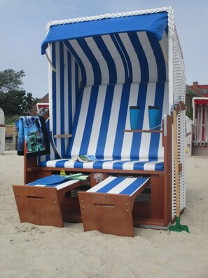 Una silla de playa con toldo a rayas, una mesita y una pala verde sobre la arena.