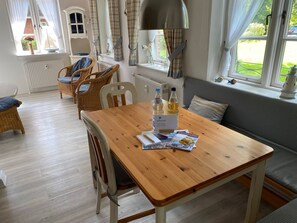 Una habitación acogedora con una mesa de madera, sillas de mimbre, un banco y una ventana con cortinas.