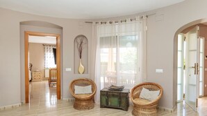 A spacious room with a tiled floor, two wicker chairs with cushions, a decorative vase, and a window with sheer curtains.