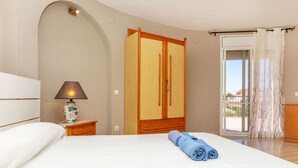 A bedroom with a bed, a nightstand, a lamp, a wardrobe, and a view through a door.