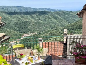 Eine Terrasse mit Esstisch, mit Blick auf eine gebirgige Landschaft.