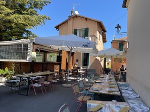An outdoor dining area with tables and chairs, umbrellas, and a building with a satellite dish.