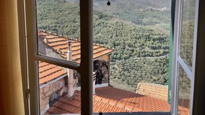Blick aus einem Fenster auf eine gebirgige Landschaft mit terrassenförmig angelegten Feldern und einem Dorf in der Ferne.